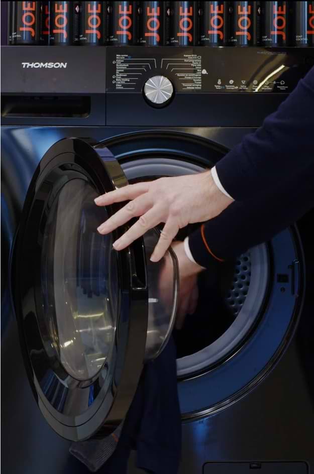 Een man met een joe trui die iets in de wasmachine doet.